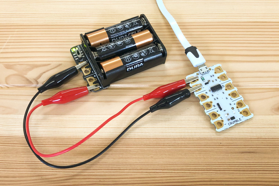 A photograph showing a battery pack connected to a Crumble controller. A black wire connects the negative terminals. A redwire connects the positive terminals.